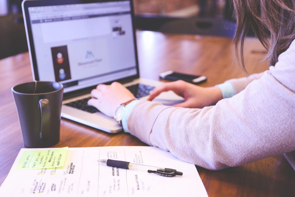 Person using laptop on desktop with notes and a pen by their side